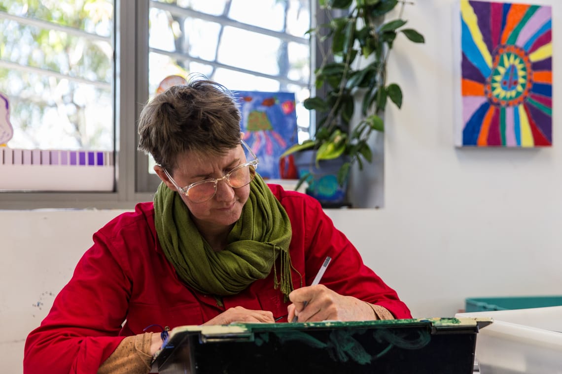 KJ sits at a desk. They are holding a pen and are busy at work.